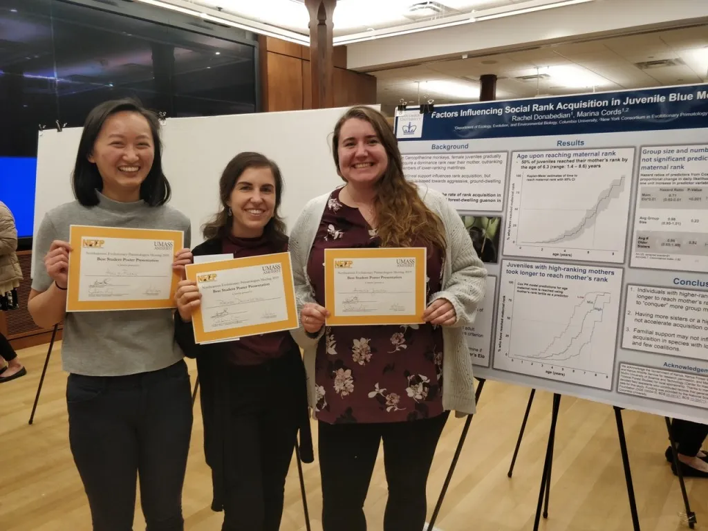 Three women standing in front of a poster holding awards