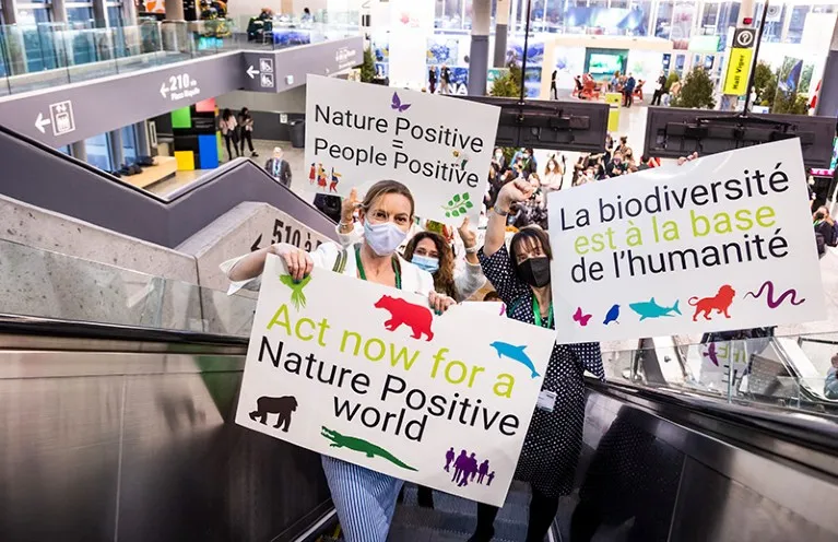 People on an escalator holding signs advocating for nature and biodiversity