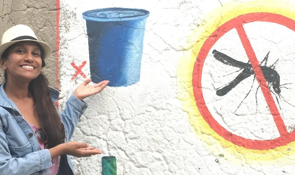 Pallavi Kache standing in front of a wall with graffiti of a bucket and a no mosquitos sign